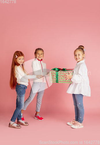 Image of Giving and getting presents on Christmas holidays. Group of happy smiling children having fun isolated on pink studio background