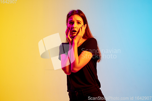 Image of Young caucasian woman\'s portrait on gradient blue-yellow studio background in neon light