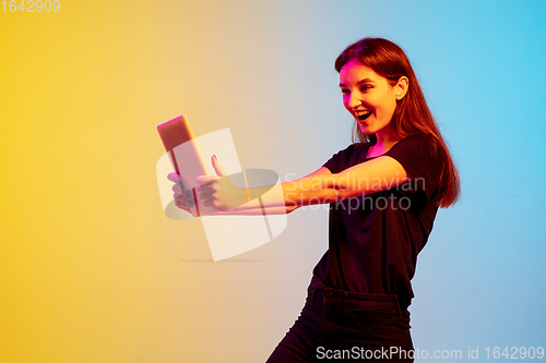 Image of Young caucasian woman\'s portrait on gradient blue-yellow studio background in neon light