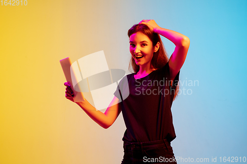 Image of Young caucasian woman\'s portrait on gradient blue-yellow studio background in neon light