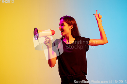 Image of Young caucasian woman\'s portrait on gradient blue-yellow studio background in neon light