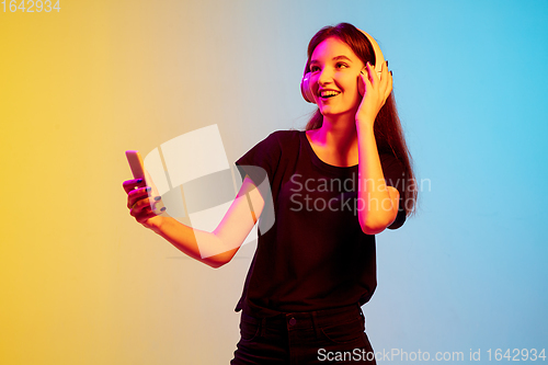 Image of Young caucasian woman\'s portrait on gradient blue-yellow studio background in neon light