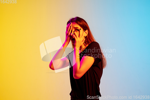 Image of Young caucasian woman\'s portrait on gradient blue-yellow studio background in neon light