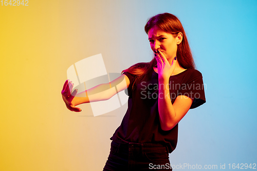 Image of Young caucasian woman\'s portrait on gradient blue-yellow studio background in neon light