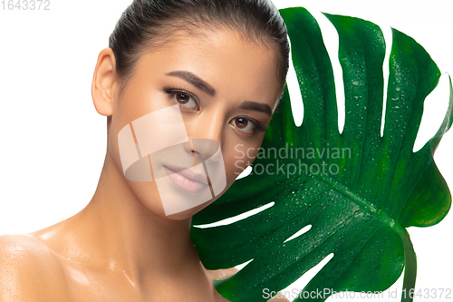 Image of Close up young woman\'s portrait with monstera leaf on white background. Cosmetics and makeup, natural and eco treatment, skin care.