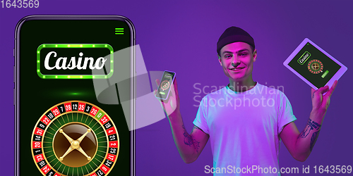 Image of Online gambling, casino concept. Young man holding devices with lottery, casino cover in neon light