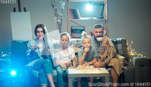 Image of Happy family watching projector, TV, movies with popcorn in the evening at home. Mother, father and kids spending time together.