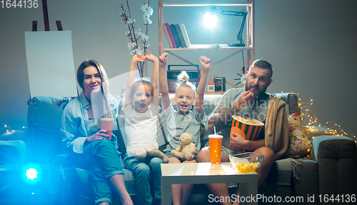 Image of Happy family watching projector, TV, movies with popcorn in the evening at home. Mother, father and kids spending time together.