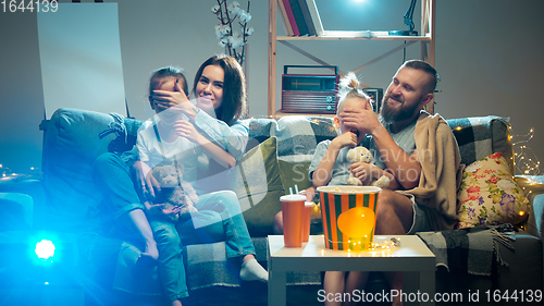 Image of Happy family watching projector, TV, movies with popcorn in the evening at home. Mother, father and kids spending time together.