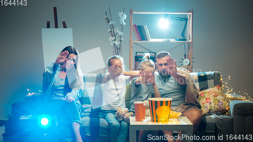 Image of Happy family watching projector, TV, movies with popcorn in the evening at home. Mother, father and kids spending time together.