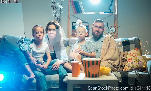 Image of Happy family watching projector, TV, movies with popcorn in the evening at home. Mother, father and kids spending time together.