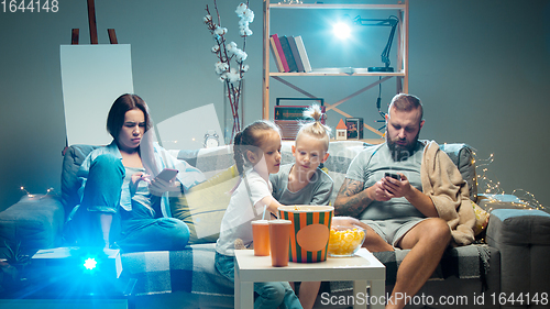 Image of Happy family watching projector, TV, movies with popcorn in the evening at home. Mother, father and kids spending time together.