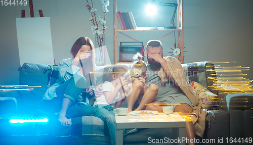 Image of Happy family watching projector, TV, movies with popcorn in the evening at home. Mother, father and kids spending time together.