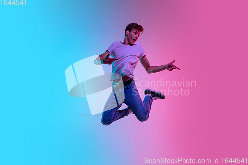 Image of Young caucasian man\'s jumping high on gradient blue-pink studio background in neon light