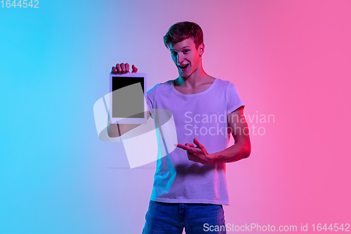 Image of Young caucasian man\'s portrait on gradient blue-pink studio background in neon light