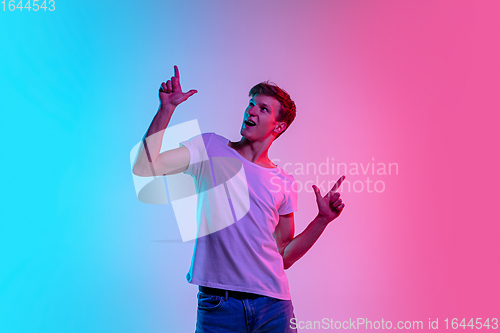 Image of Young caucasian man\'s portrait on gradient blue-pink studio background in neon light