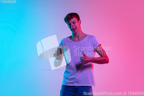 Image of Young caucasian man\'s portrait on gradient blue-pink studio background in neon light