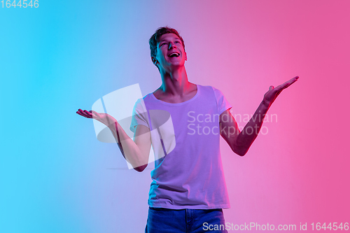 Image of Young caucasian man\'s portrait on gradient blue-pink studio background in neon light