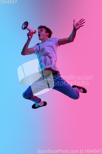 Image of Young caucasian man\'s jumping high on gradient blue-pink studio background in neon light