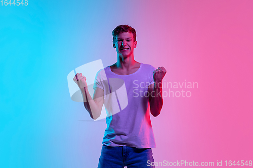 Image of Young caucasian man\'s portrait on gradient blue-pink studio background in neon light