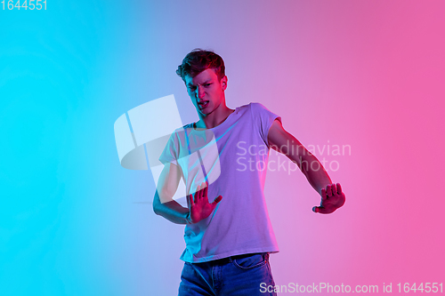 Image of Young caucasian man\'s portrait on gradient blue-pink studio background in neon light