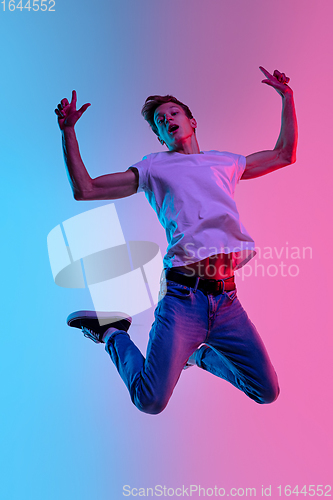 Image of Young caucasian man\'s jumping high on gradient blue-pink studio background in neon light