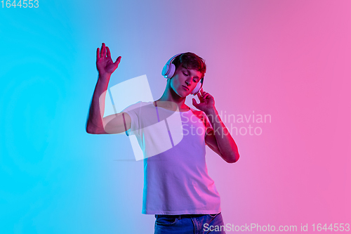 Image of Young caucasian man\'s portrait on gradient blue-pink studio background in neon light