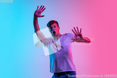 Image of Young caucasian man\'s portrait on gradient blue-pink studio background in neon light