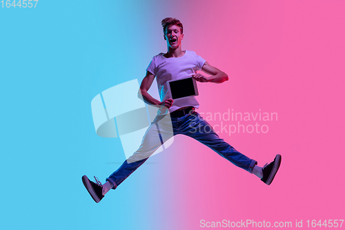 Image of Young caucasian man\'s jumping high on gradient blue-pink studio background in neon light