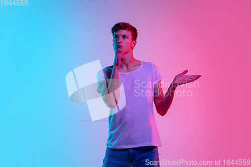 Image of Young caucasian man\'s portrait on gradient blue-pink studio background in neon light