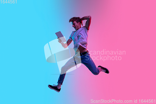 Image of Young caucasian man\'s jumping high on gradient blue-pink studio background in neon light