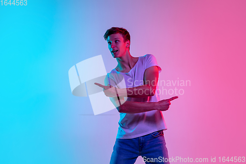 Image of Young caucasian man\'s portrait on gradient blue-pink studio background in neon light