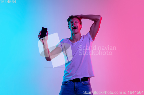 Image of Young caucasian man\'s portrait on gradient blue-pink studio background in neon light