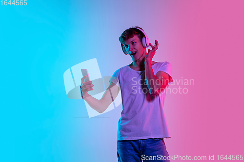 Image of Young caucasian man\'s portrait on gradient blue-pink studio background in neon light