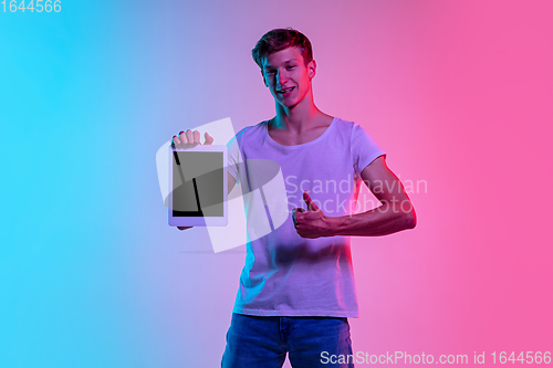 Image of Young caucasian man\'s portrait on gradient blue-pink studio background in neon light