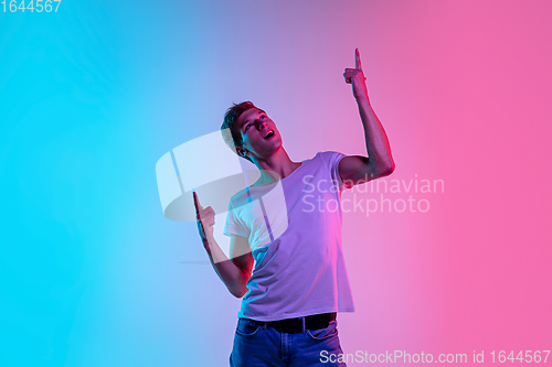 Image of Young caucasian man\'s portrait on gradient blue-pink studio background in neon light