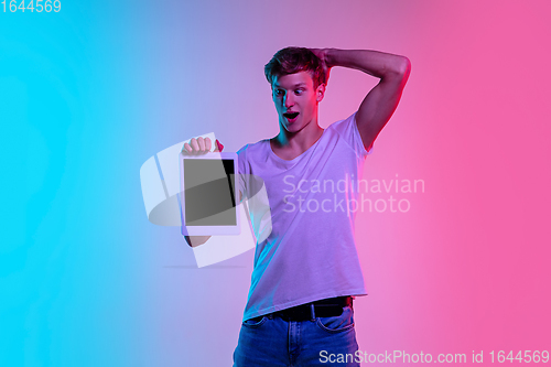 Image of Young caucasian man\'s portrait on gradient blue-pink studio background in neon light