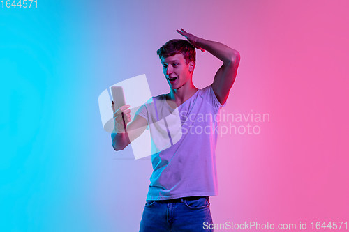 Image of Young caucasian man\'s portrait on gradient blue-pink studio background in neon light