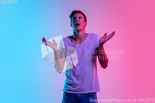 Image of Young caucasian man\'s portrait on gradient blue-pink studio background in neon light