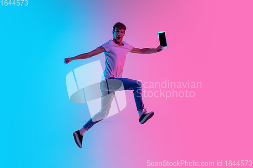 Image of Young caucasian man\'s jumping high on gradient blue-pink studio background in neon light