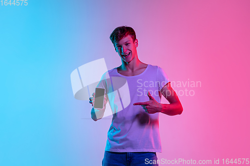 Image of Young caucasian man\'s portrait on gradient blue-pink studio background in neon light