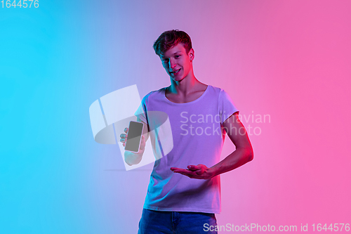 Image of Young caucasian man\'s portrait on gradient blue-pink studio background in neon light