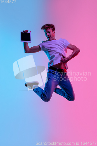 Image of Young caucasian man\'s jumping high on gradient blue-pink studio background in neon light