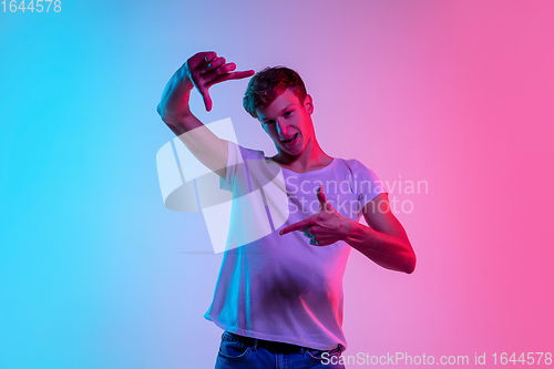 Image of Young caucasian man\'s portrait on gradient blue-pink studio background in neon light