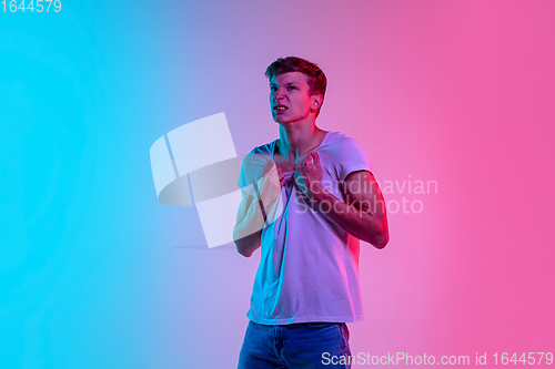 Image of Young caucasian man\'s portrait on gradient blue-pink studio background in neon light