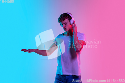 Image of Young caucasian man\'s portrait on gradient blue-pink studio background in neon light