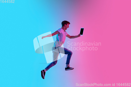 Image of Young caucasian man\'s jumping high on gradient blue-pink studio background in neon light