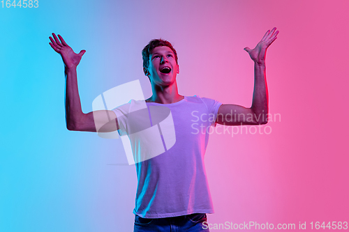 Image of Young caucasian man\'s portrait on gradient blue-pink studio background in neon light