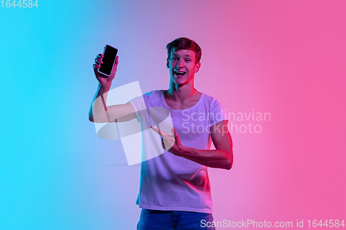 Image of Young caucasian man\'s portrait on gradient blue-pink studio background in neon light