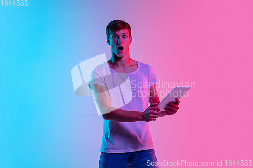 Image of Young caucasian man\'s portrait on gradient blue-pink studio background in neon light